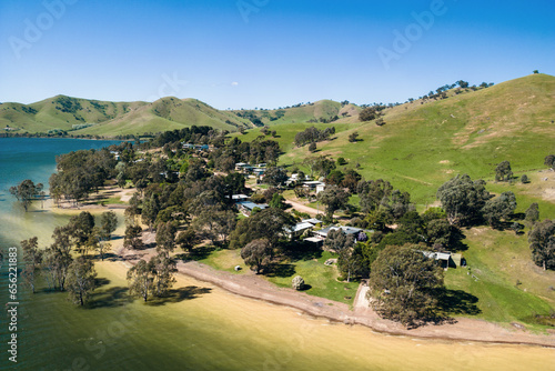 An aerial view of a small cluster of houses located on the sandy banks of Lake Eildon nestled amongst gum trees.