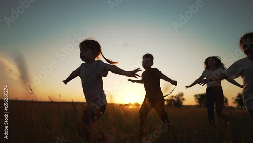 Active happy family. Group of kid run together across field at sunset.Team of kid active games in nature.Silhouette of happy children outdoors in park.Kid child run on green grass.Children family play