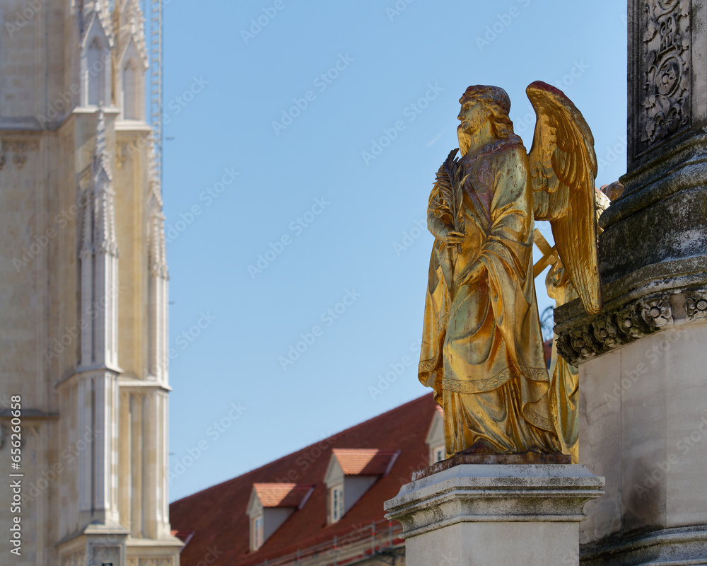 Close-up of an Angel statue placed on a column in front of Zagreb Cathedral with a clear blue sky in the background, Croatia