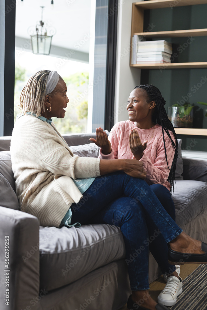 Happy african american senior mother and adult daughter sitting on couch,laughing and talking - obrazy, fototapety, plakaty 