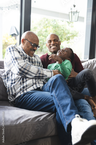 Happy african american father, son and grandfather sitting on couch,laughing and embracing