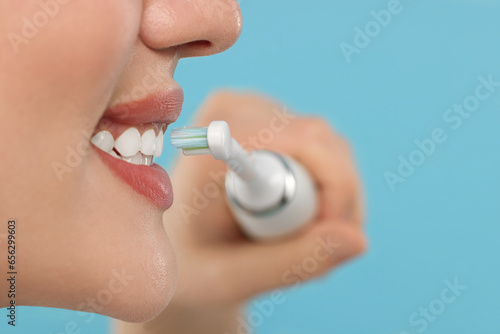 Woman brushing her teeth with electric toothbrush on light blue background, closeup. Space for text