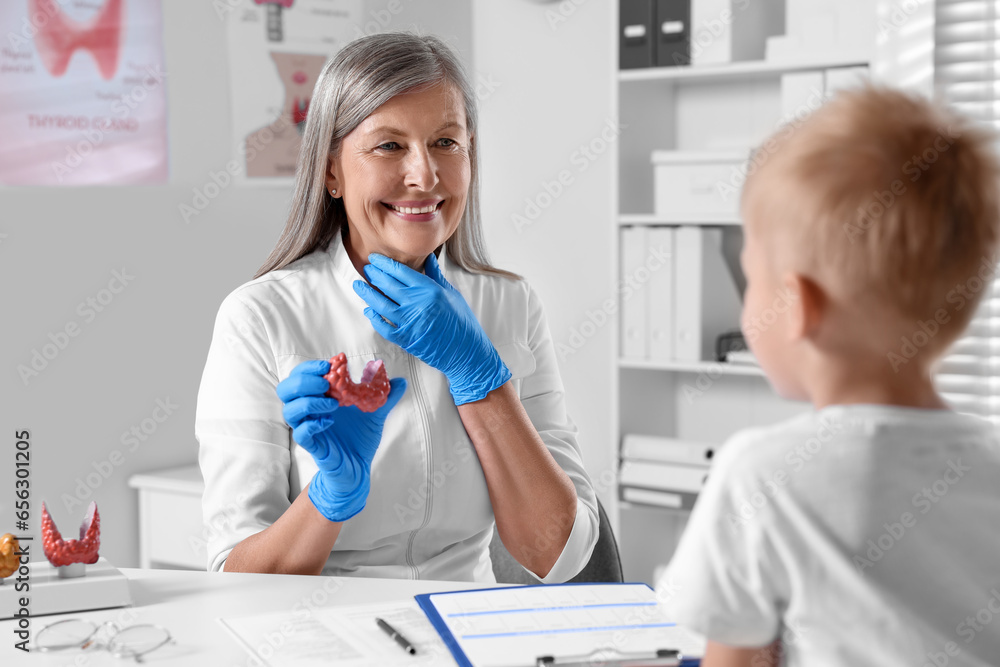 Fototapeta premium Endocrinologist showing thyroid gland model to little patient at table in hospital