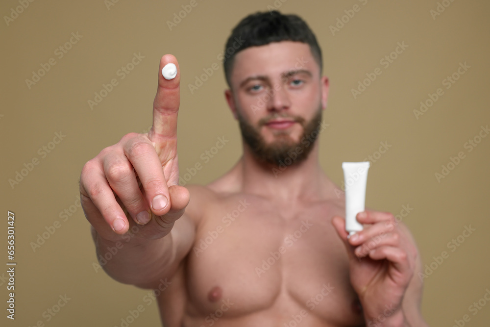 Handsome man with tube of body cream on pale brown background, selective focus Handsome man with tube of body cream on pale brown background, selective focus