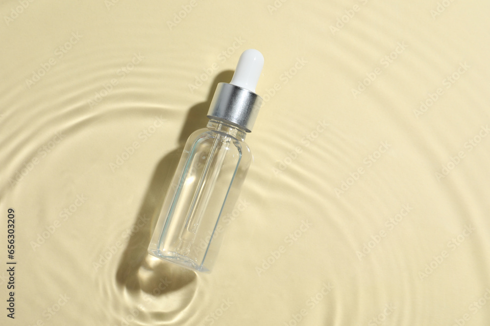 Bottle of cosmetic oil in water on beige background, top view. Space for text Bottle of cosmetic oil in water on beige background, top view. Space for text