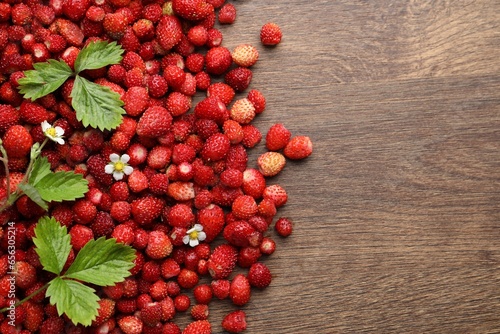 Many fresh wild strawberries, flowers and leaves on wooden table, flat lay. Space for text