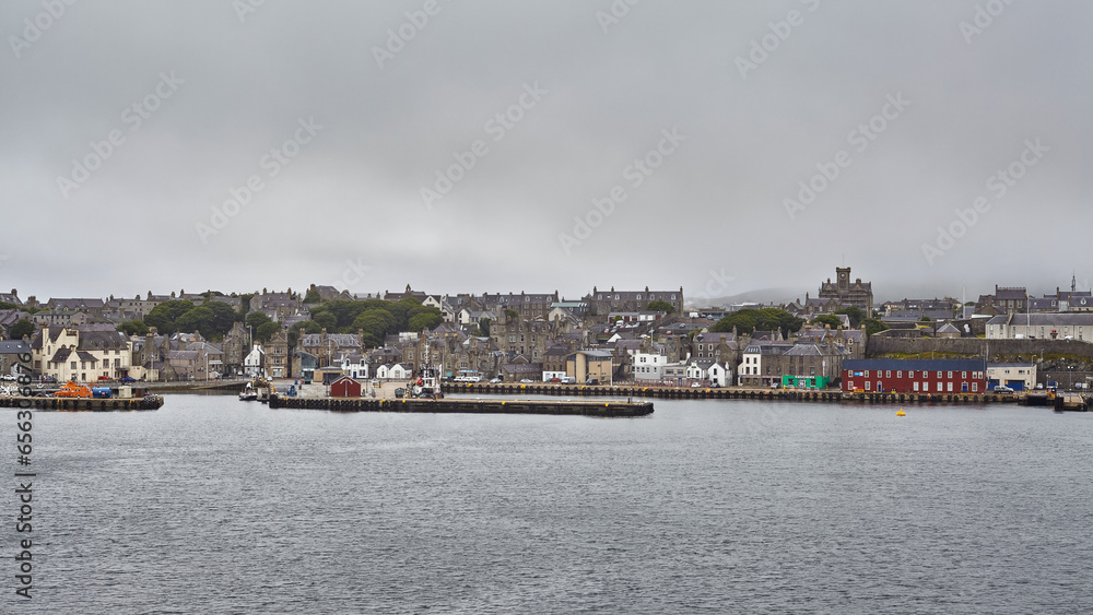 Coastal view of Lerwick city center, with calm water and grey sky.
