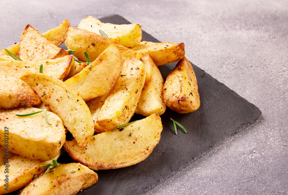 Baked potato wedges with seasonings on a stone tray on a gray stone. Baked potato wedges with seasonings on a stone tray on a gray stone.