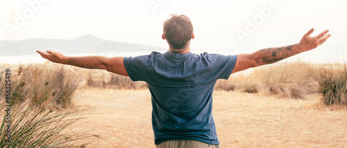 Happiness and freedom travel people lifestyle. One man back view outstretching arms overjoy and excited admiring amazing journey adventure destination in background with ocean and island. Joyful life