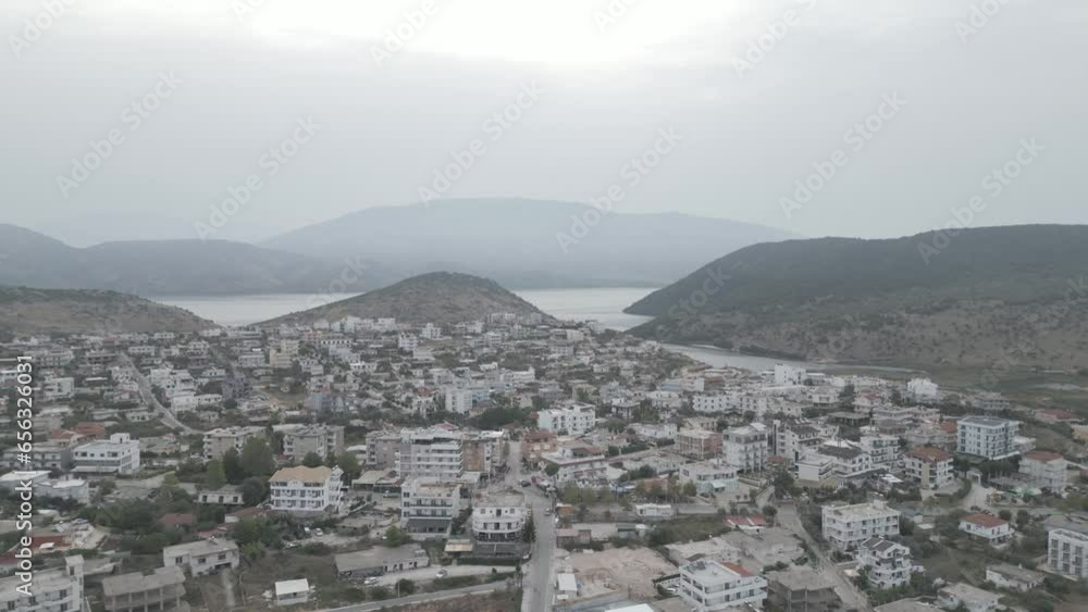 Drone shot flying over Ksamil Albania in the morning on a cloudy grey day with haze in the sky and white hotels and houses in the background with mountains and the sea LOG Drone shot flying over Ksamil Albania in the morning on a cloudy grey day with haze in the sky and white hotels and houses in the background with mountains and the sea LOG