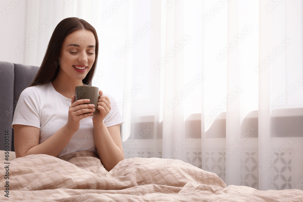 Beautiful woman with cup of drink on bed at home, space for text. Lazy morning Beautiful woman with cup of drink on bed at home, space for text. Lazy morning