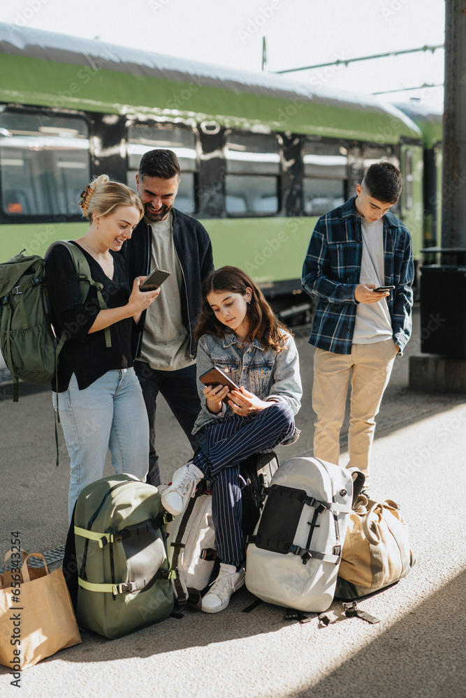 Family using smart phones while waiting for train at railroad station Family using smart phones while waiting for train at railroad station