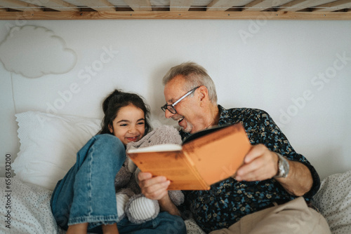 Happy senior man reading storybook with granddaughter on bed at home photo