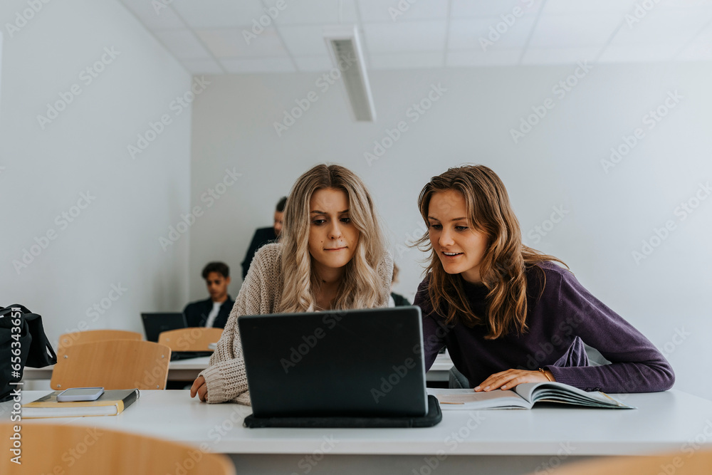 Young female students using laptop together at desk in classroom Young female students using laptop together at desk in classroom
