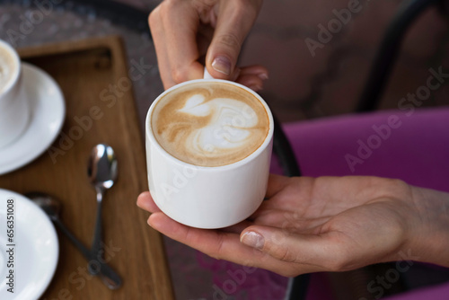 white ceramic cup of cappuccino in woman's hands over glass coffee table 
