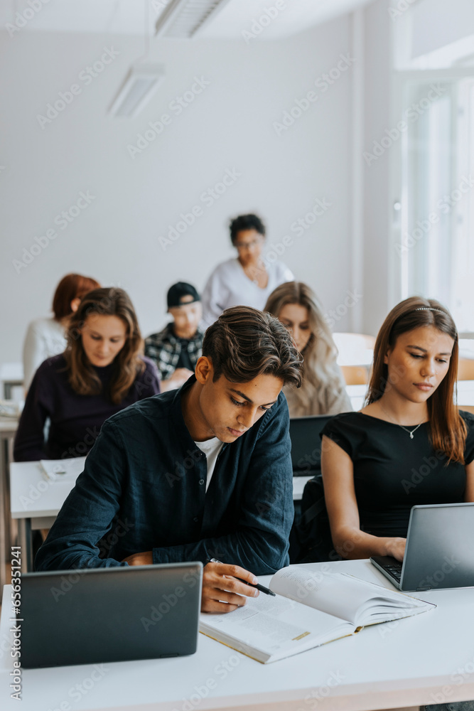 Male and female students sitting at desk while studying in classroom Male and female students sitting at desk while studying in classroom