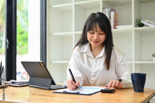 Pretty asian female employee, accountant checking report, financial data or bookkeeping at desk. Finances and economy concept