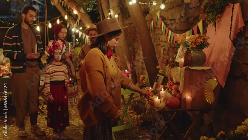 Medium shot of modern Latin family in festive outfits coming up to beautifully decorated altar one by one and lighting up candle in honor of their departed family member on Day of the DeadMedium shot 