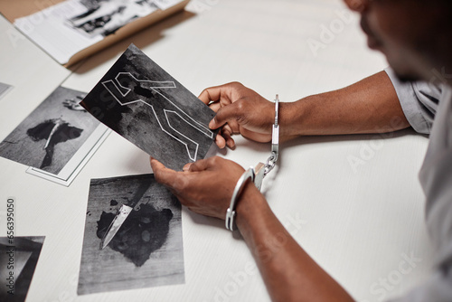 Closeup of man wearing handcuffs looking at evidence pictures during interrogation in police department, copy space
