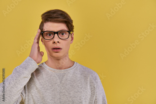 shocked man in white sweatshirt touching glasses and slightly opening his mouth on yellow backdrop