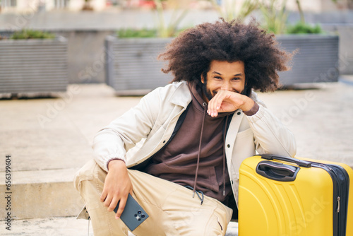 Smiling African-American man, with afro hairdo, sitting leaning on suitcase