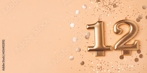 Photography Gold candles in the form of number twelve on peach background with confetti