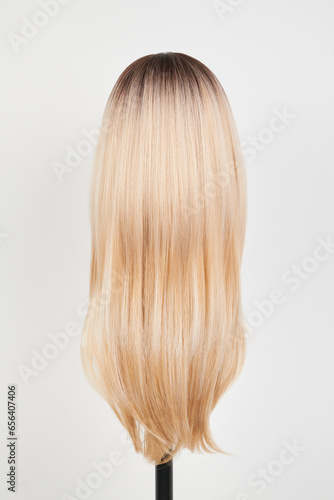 Natural looking blonde wig on white mannequin head. Long hair on the plastic wig holder isolated on white background  back view.