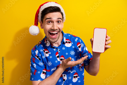 Portrait of handsome astonished guy demonstrate empty space samrt phone screen proposition isolated on yellow color background photo