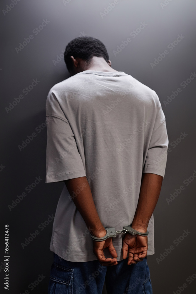 Back view of young Black man arrested standing by wall with handcuffs Back view of young Black man arrested standing by wall with handcuffs