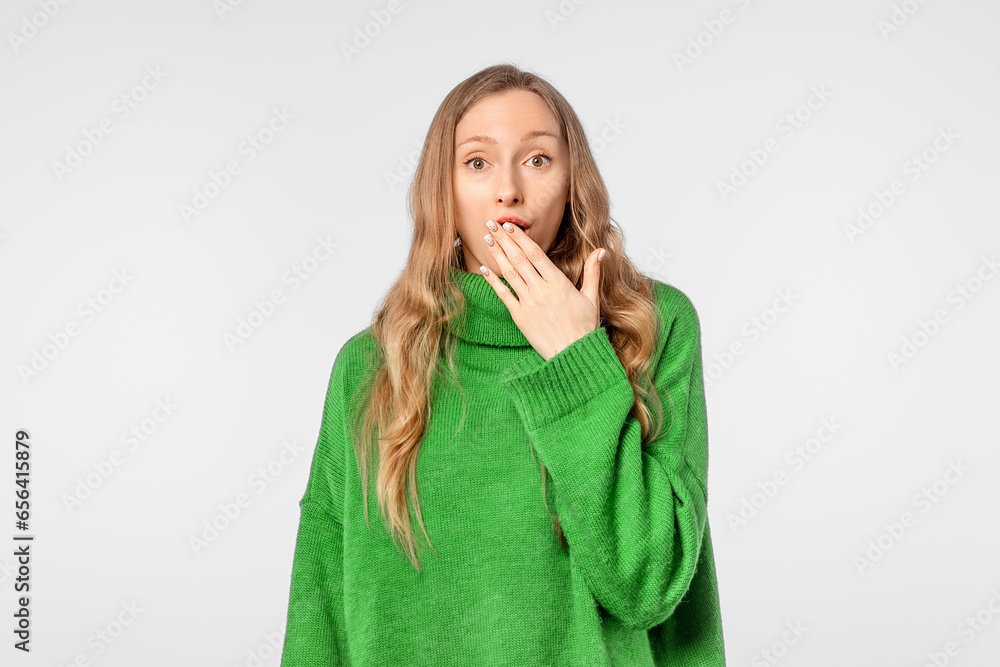 Amazed young woman showing Oops expression at the camera, arm cover mouth, wearing soft green sweater, standing over neutral background Amazed young woman showing Oops expression at the camera, arm cover mouth, wearing soft green sweater, standing over neutral background