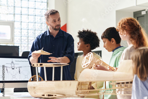 Tutor explaining group of children how to make plane out wooden parts photo