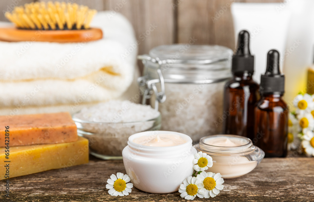 Chamomile spa. Composition with chamomile flowers, handmade soap, essential oil cosmetic bottle, body cream, scrub and sea salt on a white texture background. Relaxing beauty treatments.Copy space