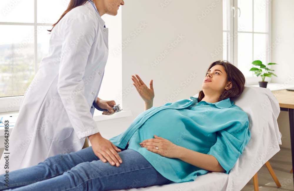 Pregnancy, gynecology, medicine, health care and people. Pregnant woman is talking to female gynecologist doctor during routine checkup at hospital. Pregnant woman is lying on couch in doctor's office