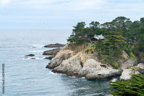 California, USA - May 19, 2018: lone cottage villa house surrounded by cypress trees at seaside cliff on pacific coastline with blue ocean and sky of big sur in usa