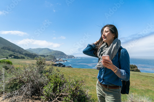 happy asian chinese lady visitor enjoying California sun and breeze with phone in hand at beautiful big sur park in usa
