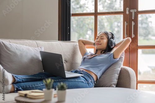 Woman listening music in headphones while lying on sofa in room
