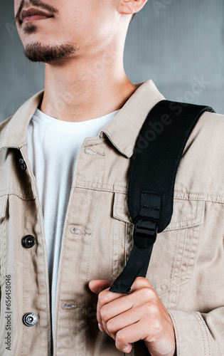 A black backpack is hanging on the shoulder of a guy in a light jacket