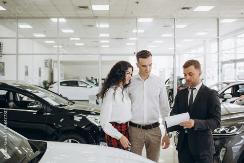 Couple and the dealer selling cars look the car in the showroom. photo