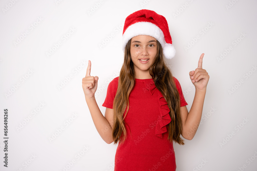Cute little girl in santa hat pointing fingers up standing isolated over white background. Cute little girl in santa hat pointing fingers up standing isolated over white background.
