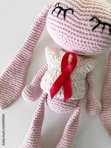 Children's toy bunny with a raspberry ribbon for children's cancer awareness on a white background. Children's Cancer Day, February 15th.