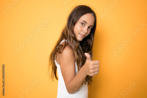 Portrait of child girl showing thumb up isolated over yellow background.