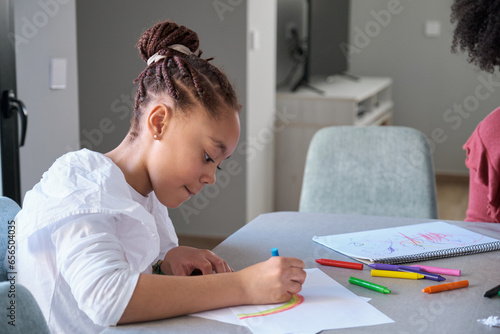 Braided hair girl painting a rainbow at home. Preteen girl drawing on her freetime.