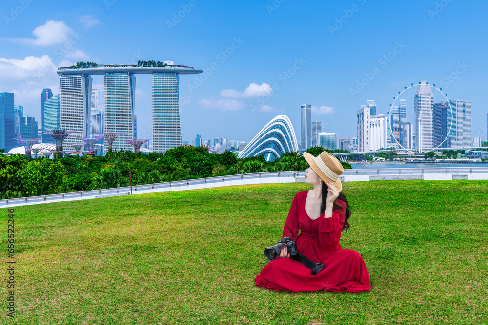 Tourist girl in a red dress Sit on the green grass at Marina barrage park Singapore.