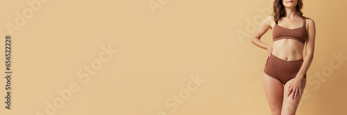 Cropped image of female body in brown underwear against beige studio background. Banner. Concept of body and skin care, fitness, natural beauty, health, wellness. Copy space for ad