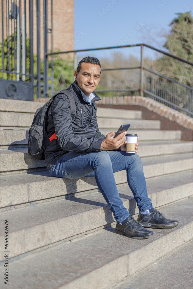 Latino man in sitting on some stairs using his mobile phone. Latino man in sitting on some stairs using his mobile phone.
