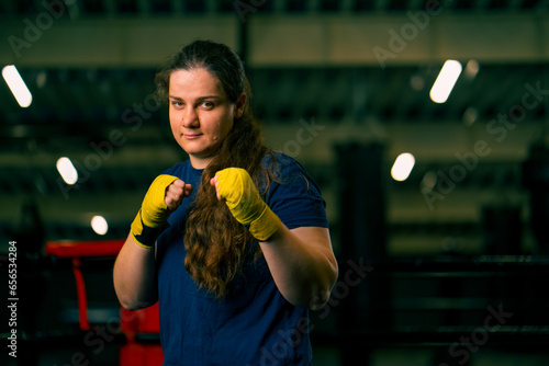 portrait focused Boxer girl in yellow boxing bandages standing in a boxing stance on a dark background in a gym before a fight
