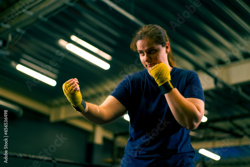 portrait focused Boxer girl in yellow boxing bandages standing in a boxing stance on a dark background in a gym before a fight