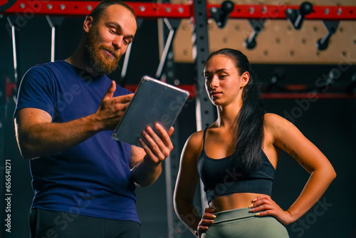 a male trainer holds a tablet in his hands and shows a training schedule to a female athlete preparing her body for the competition