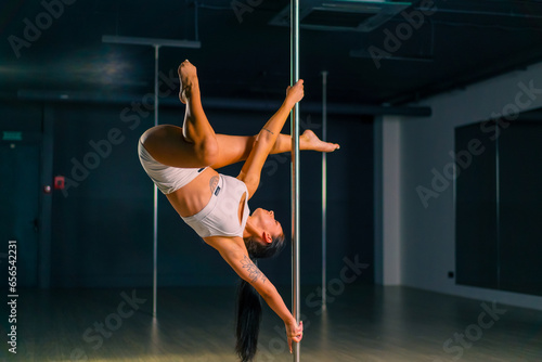 Flexible girl doing gymnastic exercises on a pole for stretching Beautiful sexy woman showing body Pole dance sport