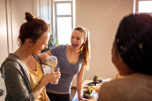 Young woman pouring a healthy shake for her friend in the kitchen photo
